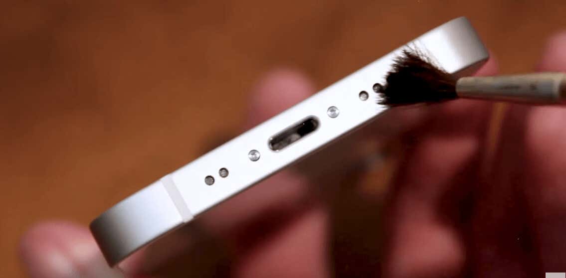 Person cleaning an iPhone's speaker with a small brush