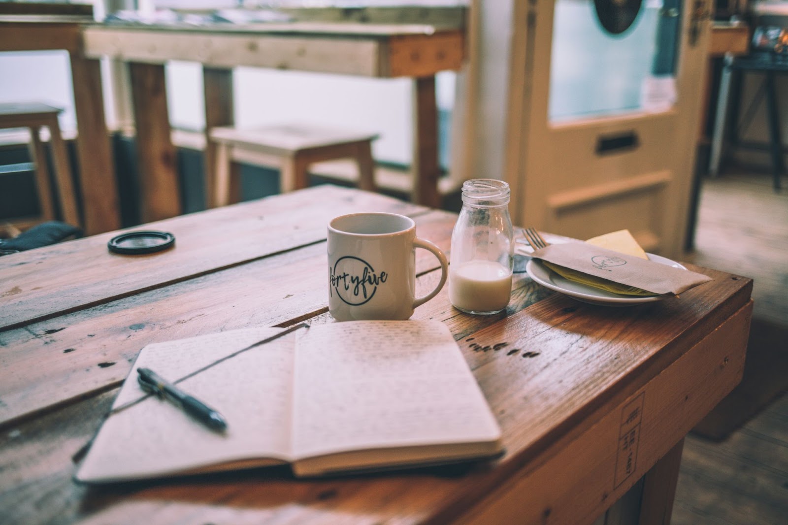 Open notebook on a table next to a mug and bottle of milk