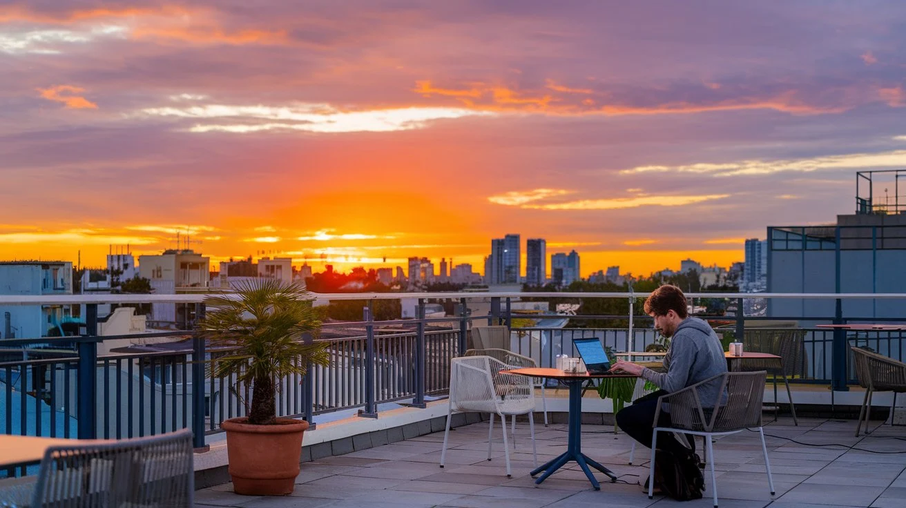 Digital nomad typing on a laptop at a rooftop café during sunset.