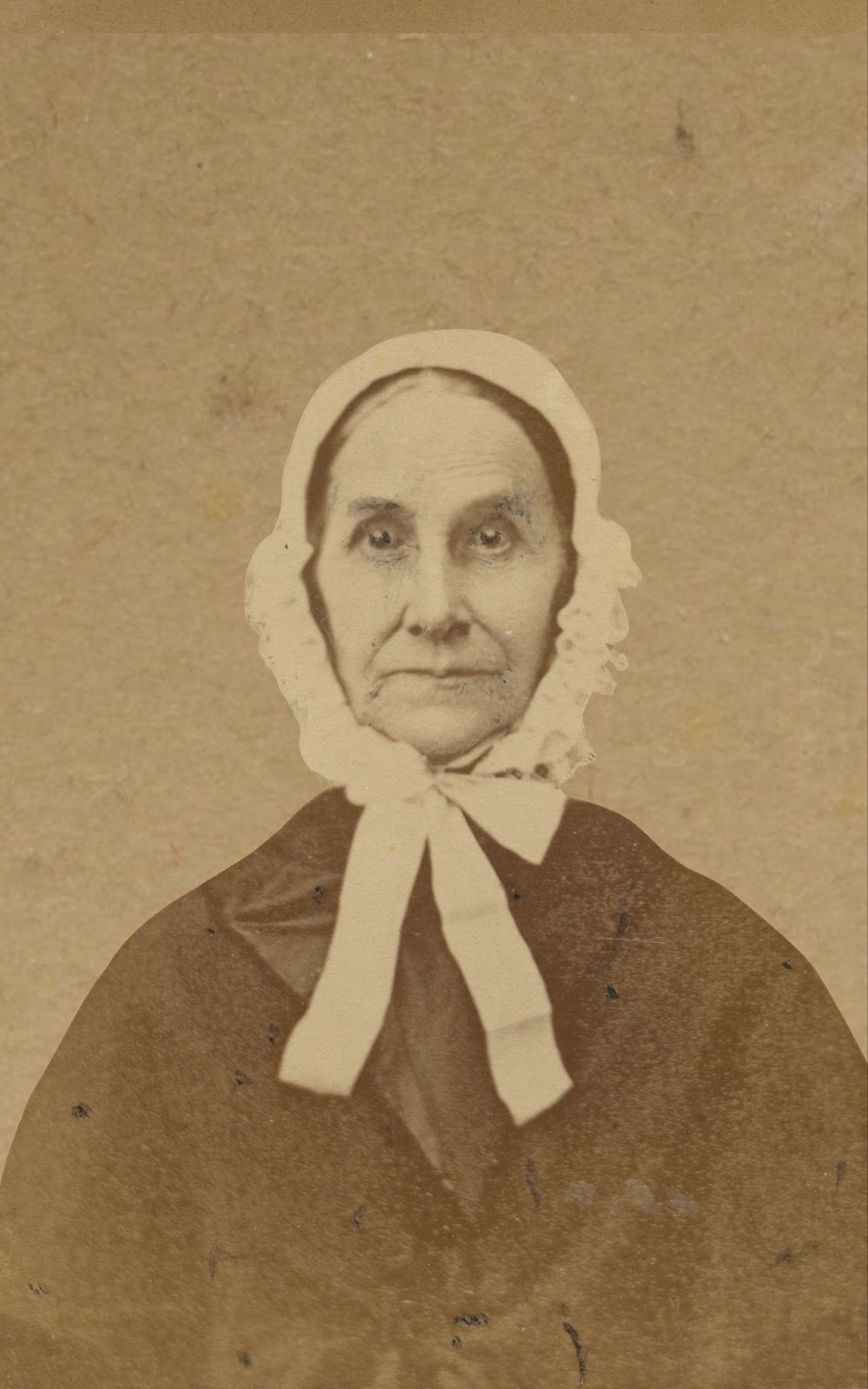 An historic black & white photo of a serious-faced woman wearing a light-colored bonnet and starting straight at the camera
