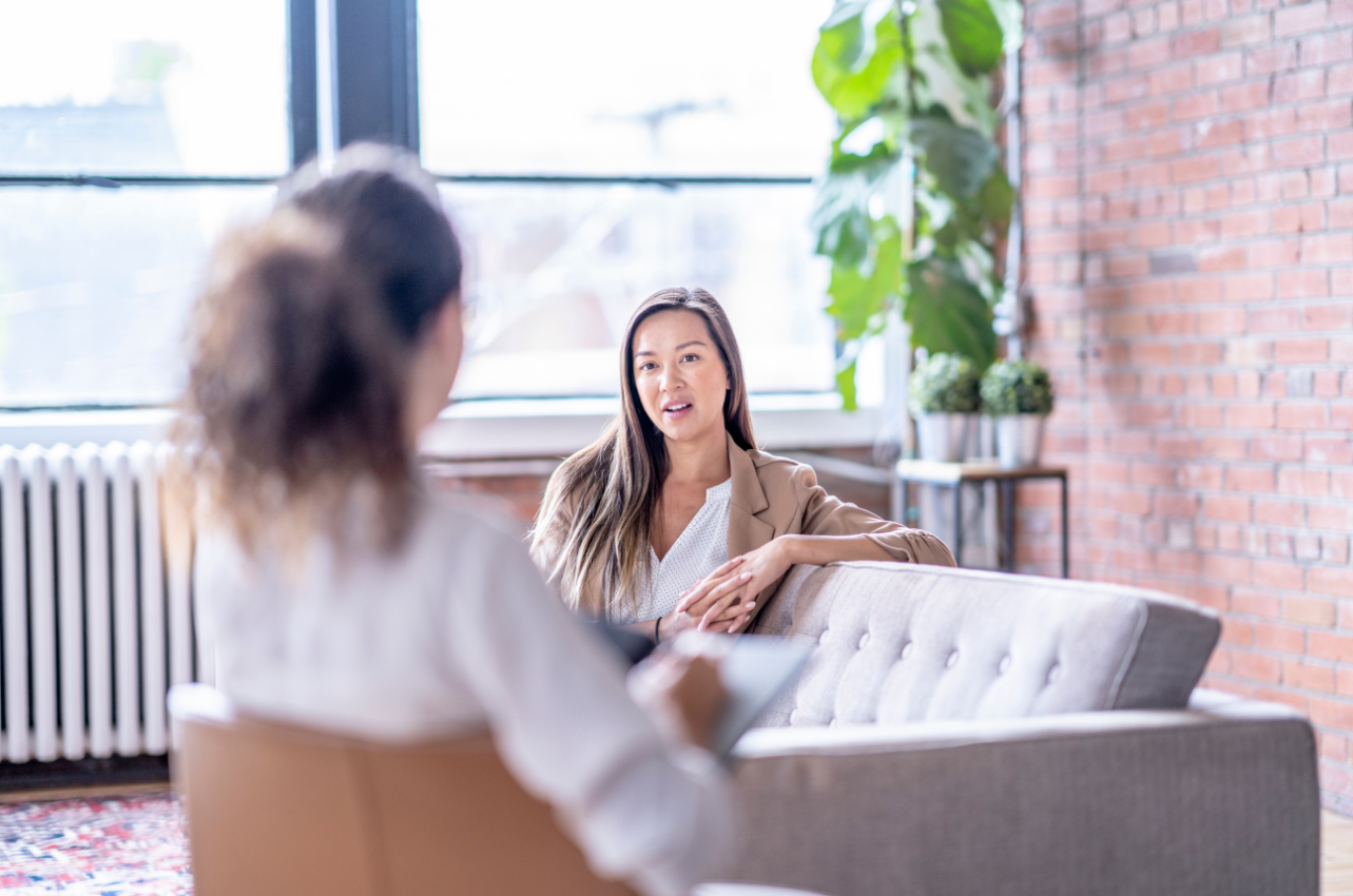 Woman talking to therapist in brick room with big windows and pot plants // Healthier Baby Today