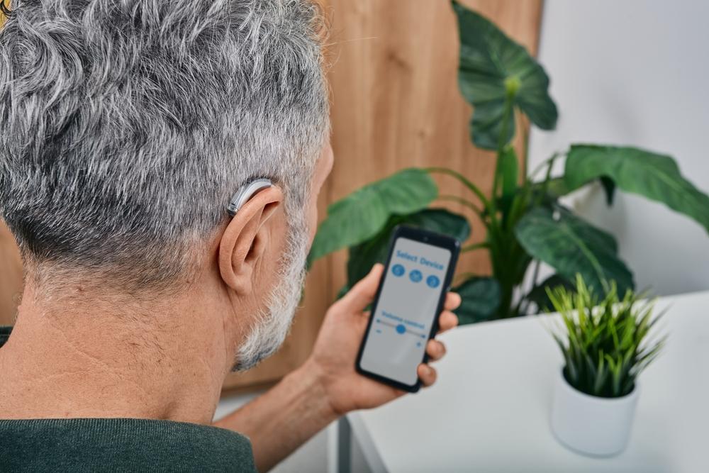 man adjusting hearing aids with mobile device
