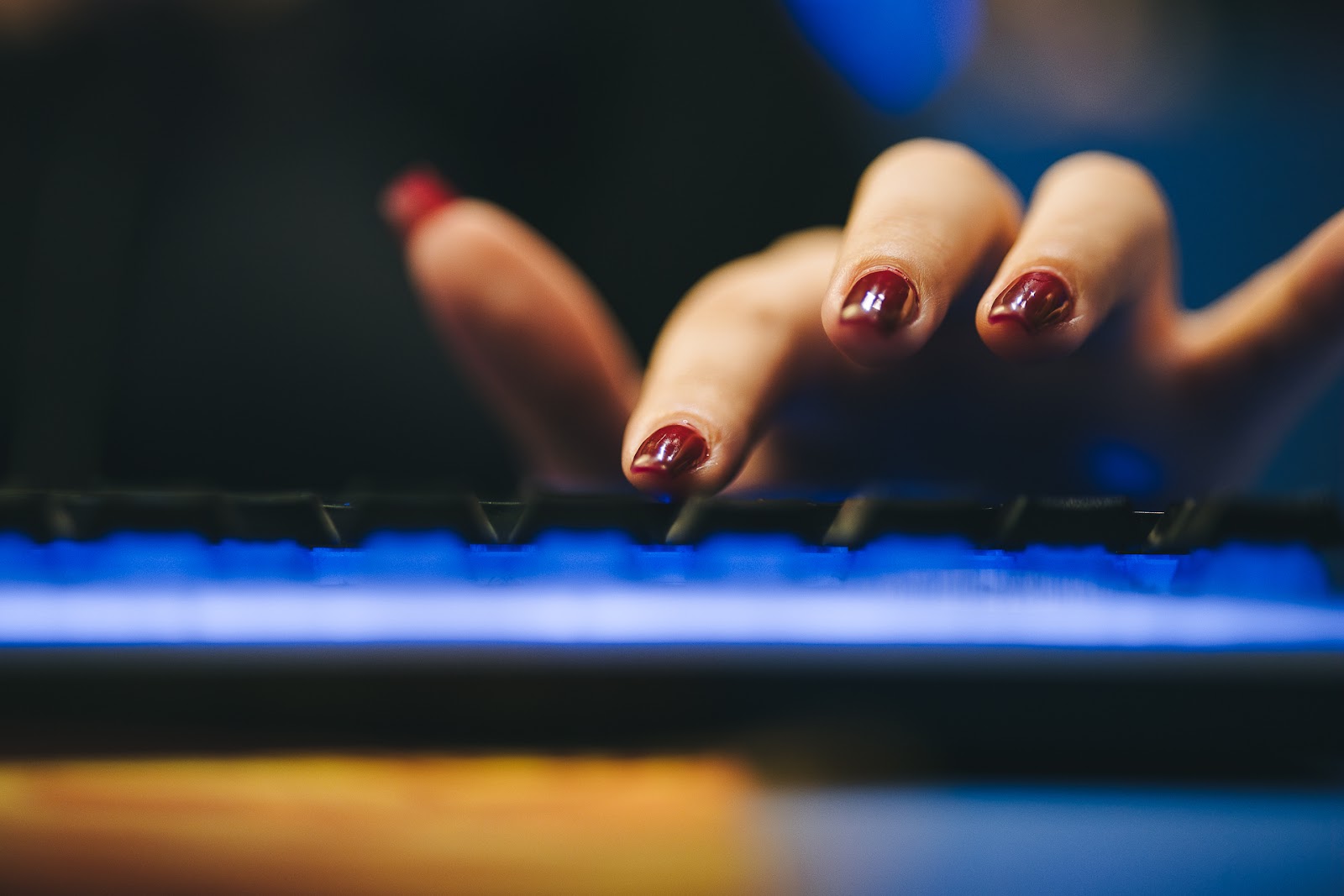 Foto focada em mãos manuseando um teclado. Unhas pintadas induzem que trata-se de uma mulher praticante de e-sports.