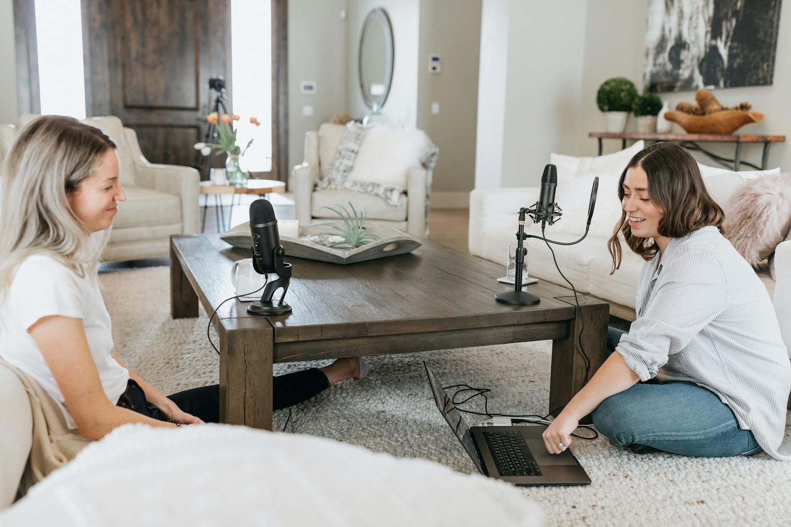 Two women sitting on floor, with microphones, ready to record a Podcast