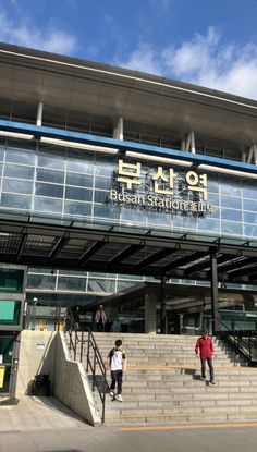 This contains a picture of  two people are standing on the steps outside KBS Busan building