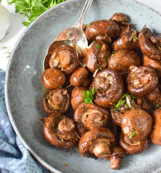 Whole mushrooms in grey bowl with a serving spoon