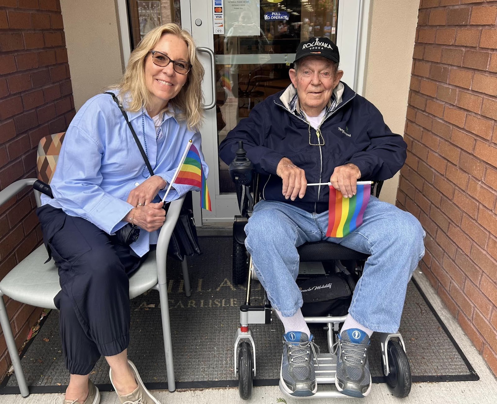 A woman and an old man with rainbow flags smiling at the camera