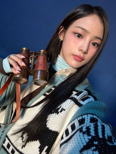 This contains a picture of Minji with long black hair holding a pair of binoculars