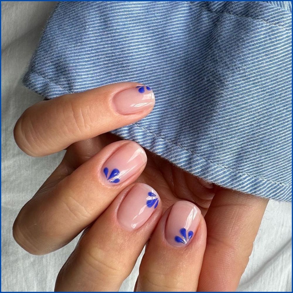 Close up of hands with flowered designed blue nails having petals on nude nails