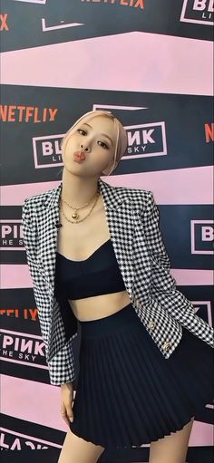 This contains an image of 
BLACKPINK's Rosé wearing a skirt and jacket in front of a wall with advertisements