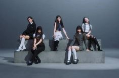 This may contain: four young women sitting on top of a cement bench in front of a gray background