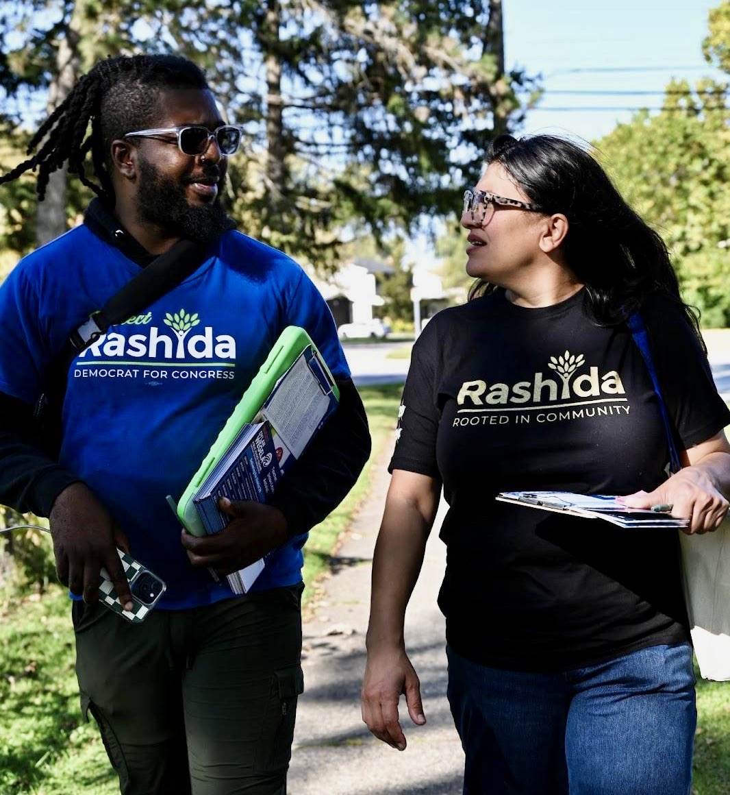 Rashida and Joshua hold clipboards and walk through the streets of the 12th district.