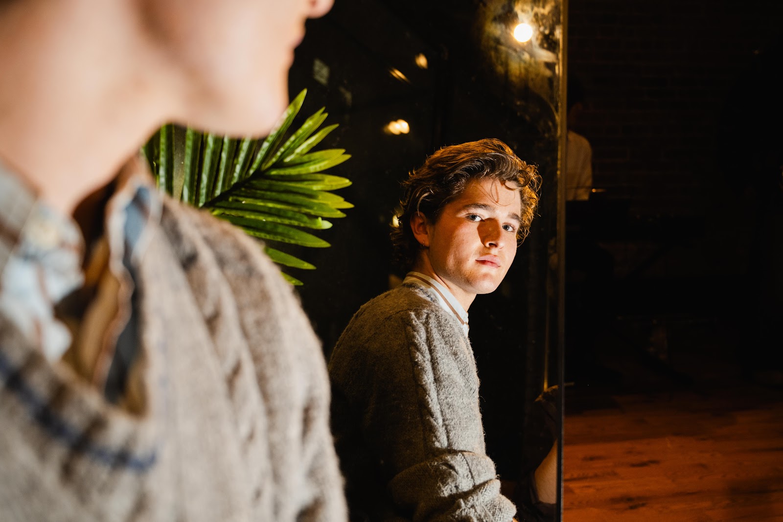 Matthew Cosgrove looks into a mirror at the camera in a dim backdrop under warm light. 