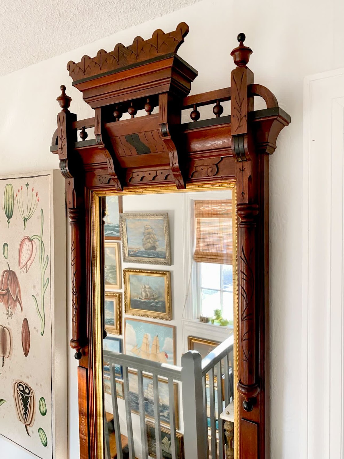 An Eastlake mirror hung on the wall reflects a gallery wall full of ship paintings hung alongside the stairway.