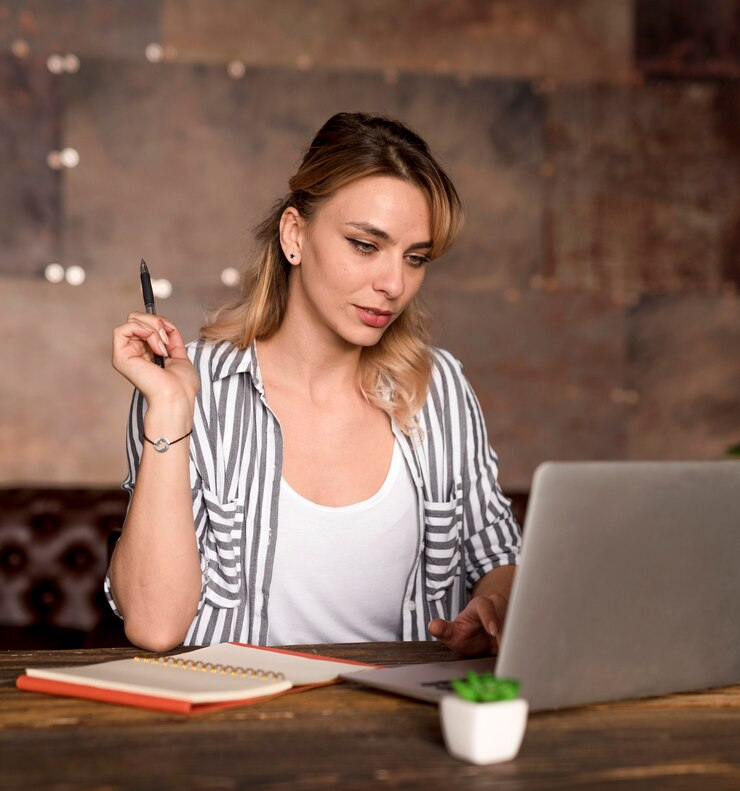 A woman researching ideas on a laptop with an open notebook beside her