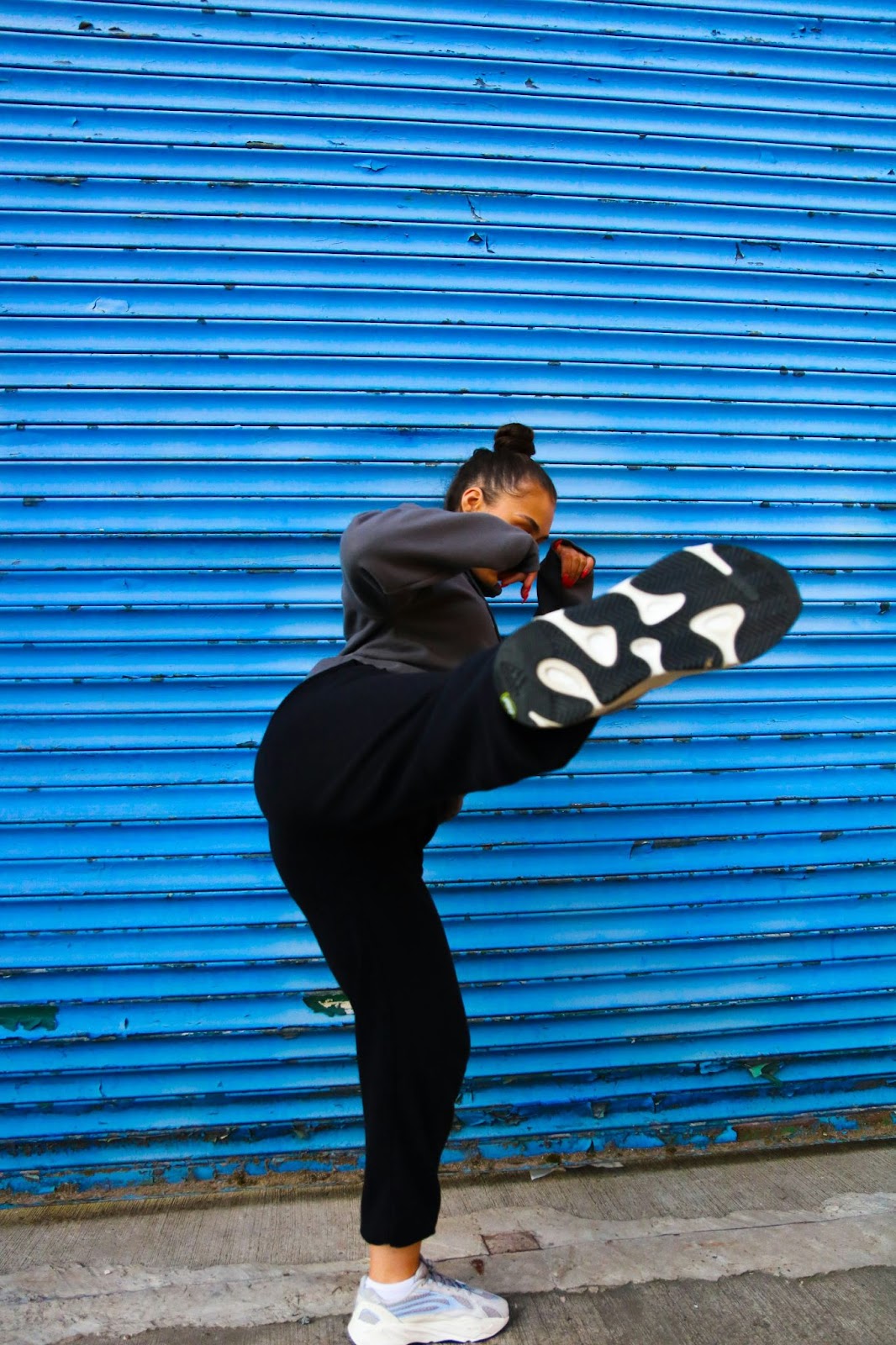 A woman throwing a kick in front of a blue wall.