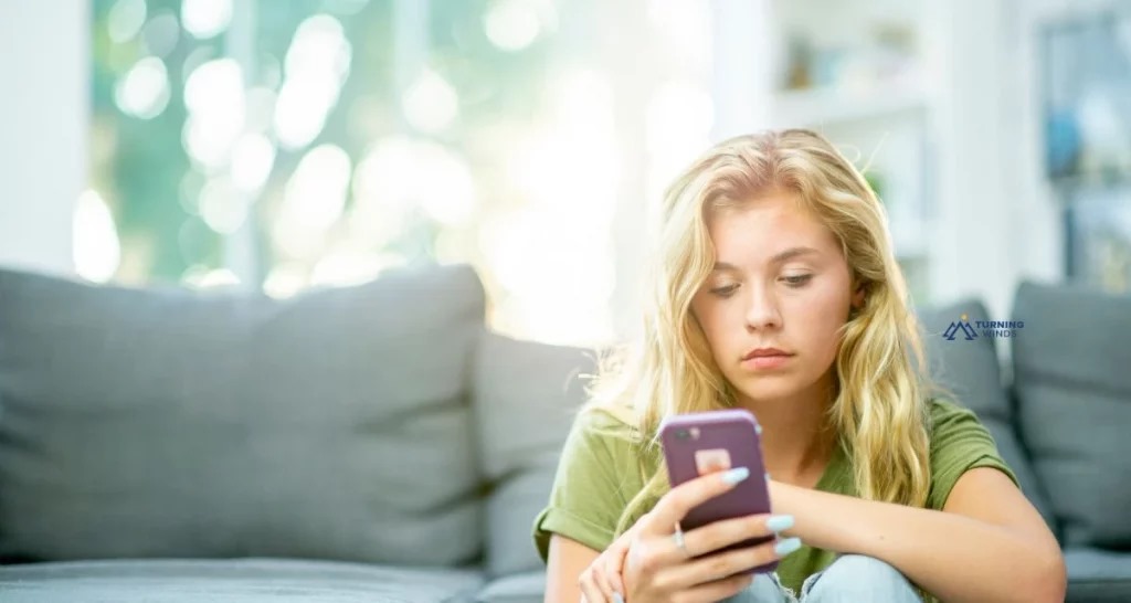 A blonde woman using her phone, appearing distracted and thinking about how to quit social media without quitting.