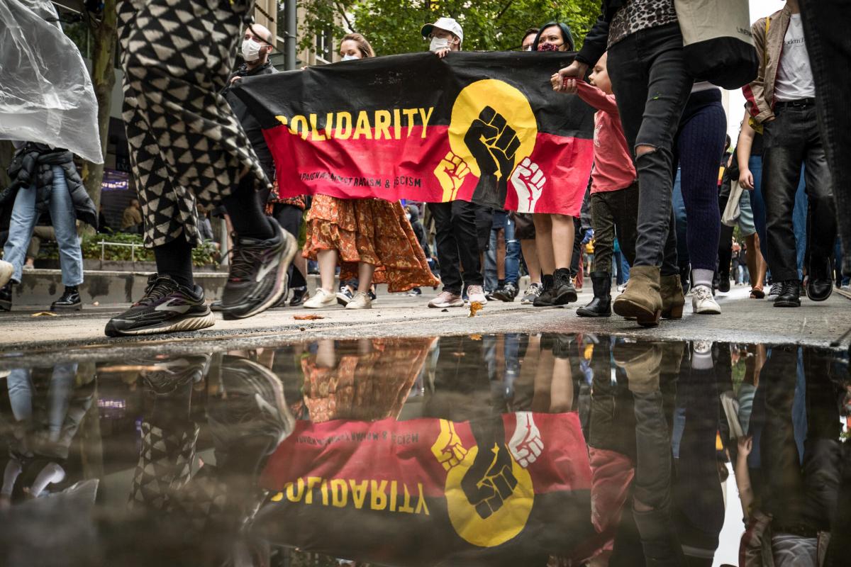 A picture of a protest showing an Aboriginal flag with Solidarity written in the middle of the flag.