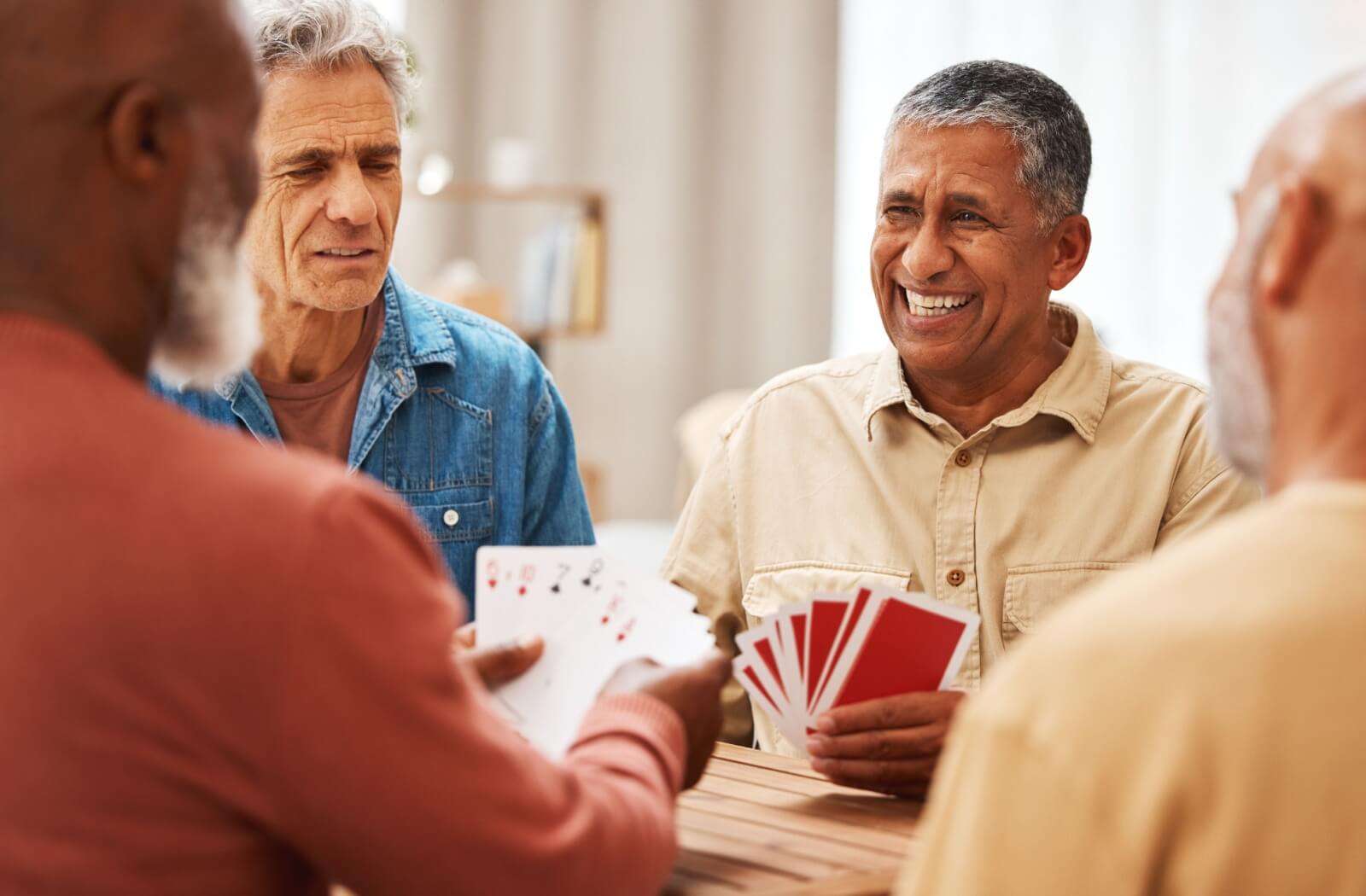 Group of seniors smiling and playing cards around a table, showcasing social activities in a welcoming assisted living community