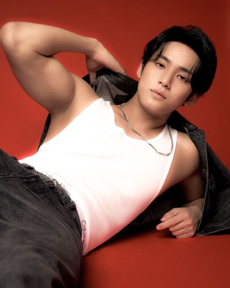 This contain an image of MINGYU  laying on the ground with his hands behind his head, wearing jeans and a white tank top