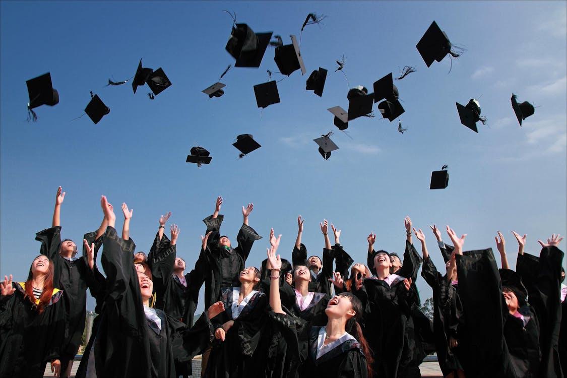 Free Group of graduates celebrating by throwing caps in the air during a sunny day. Stock Photo