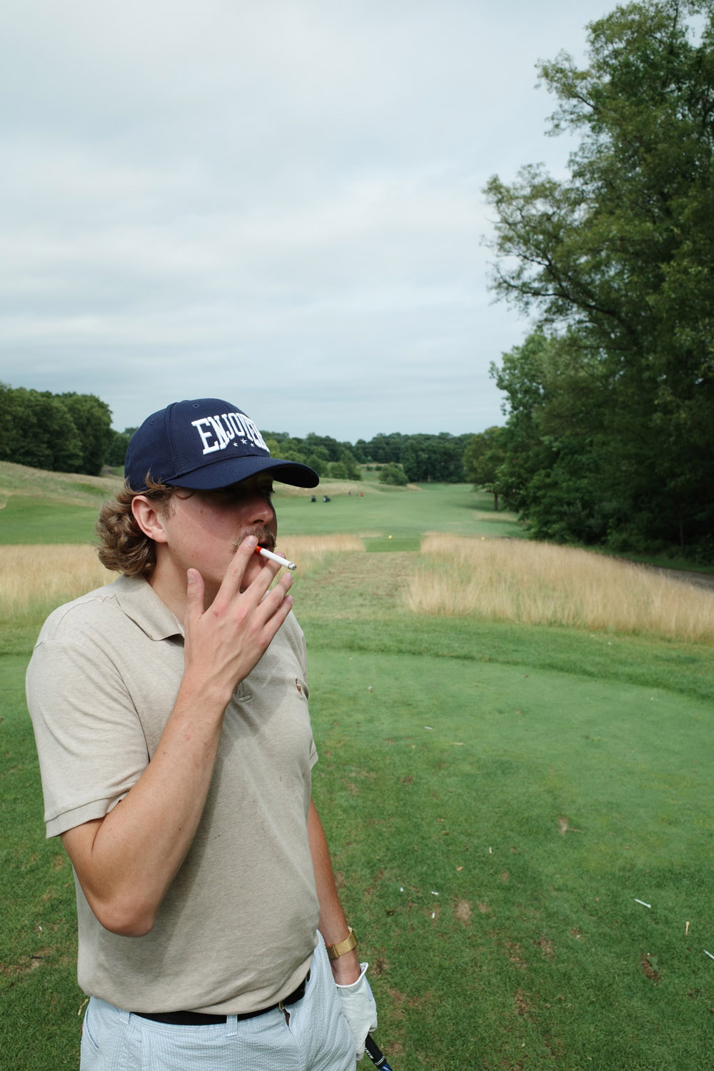 Bobby Mars smoking a Hestia cigarette on the tee box in Enjoyer hat.