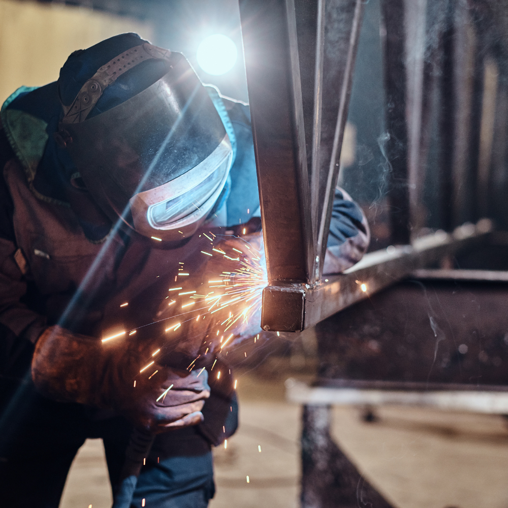 Saldatore professionale al lavoro durante un processo di saldatura certificato con protezioni di sicurezza e scintille visibili.