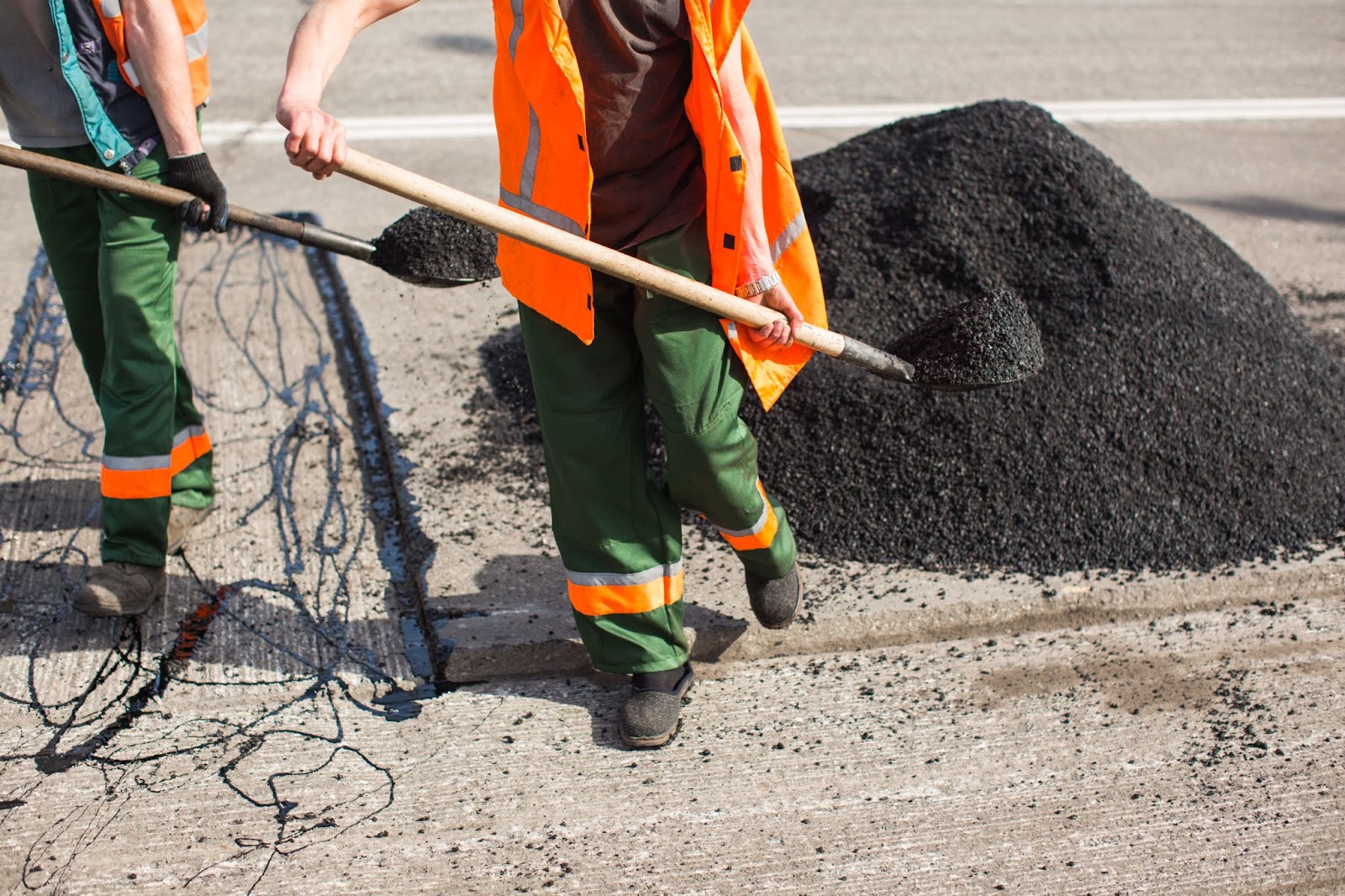 An image of a road under repair with construction workers shoveling black concrete. 