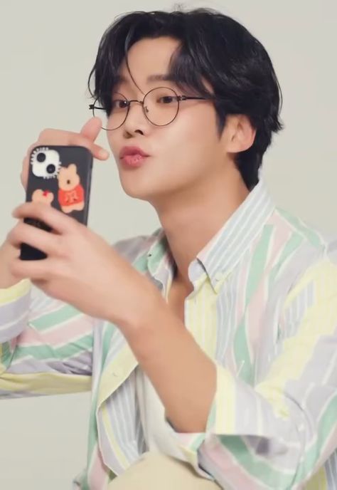 This contain Rowoon is taking a selfie with his cell phone while wearing glasses and a striped shirt