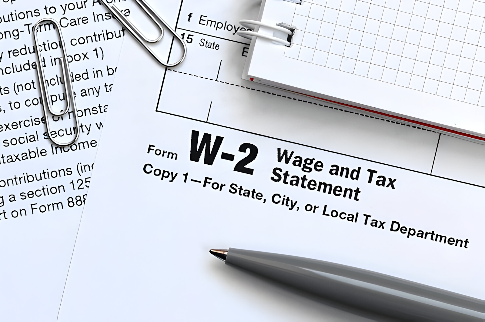 A close-up of a W-2 Wage and Tax Statement form, accompanied by a pen and paperclips, representing the process of managing payroll services.







