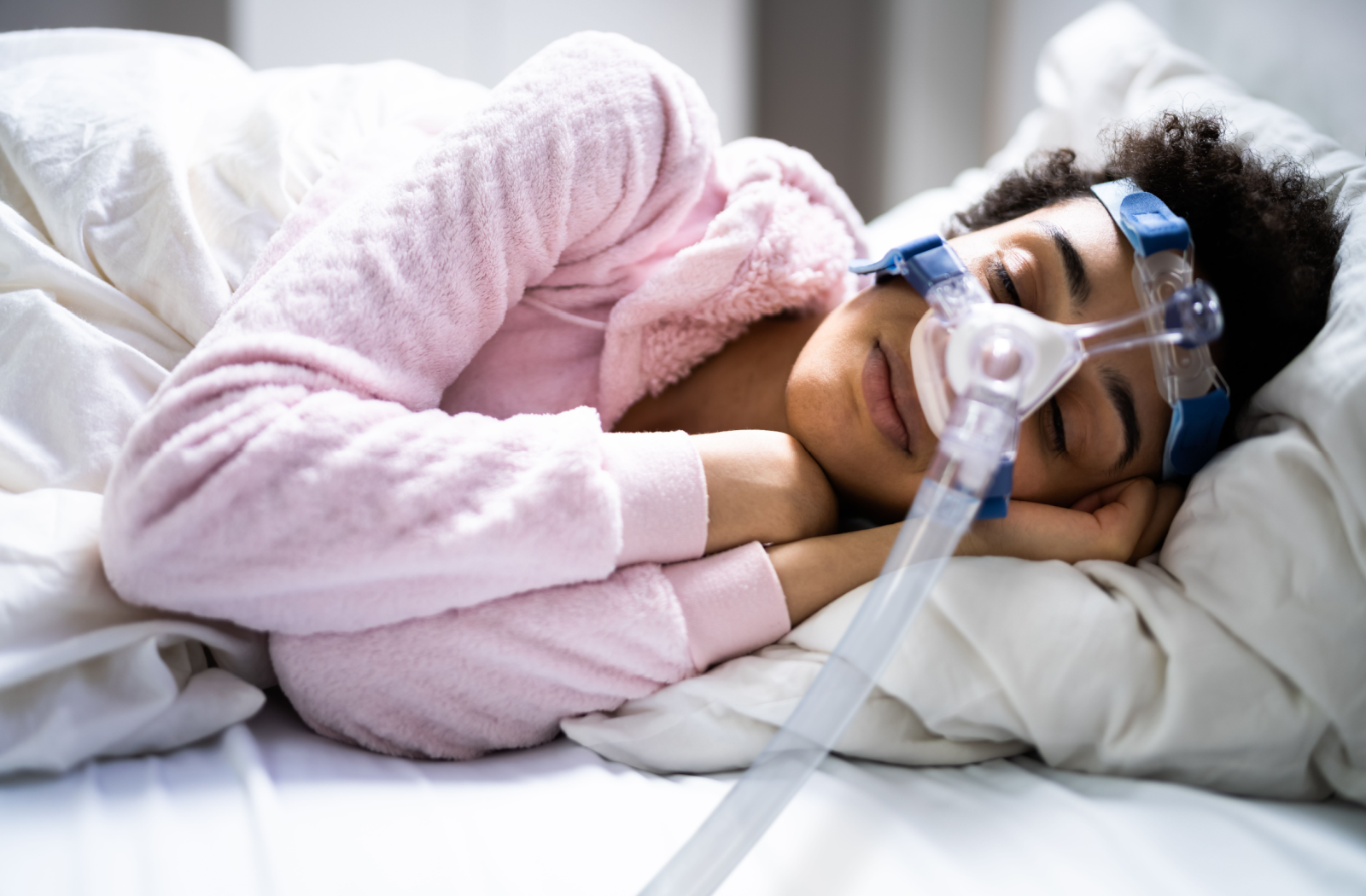 A person in a cozy bed curls up with a CPAP machine, helping them breathe while sleeping.