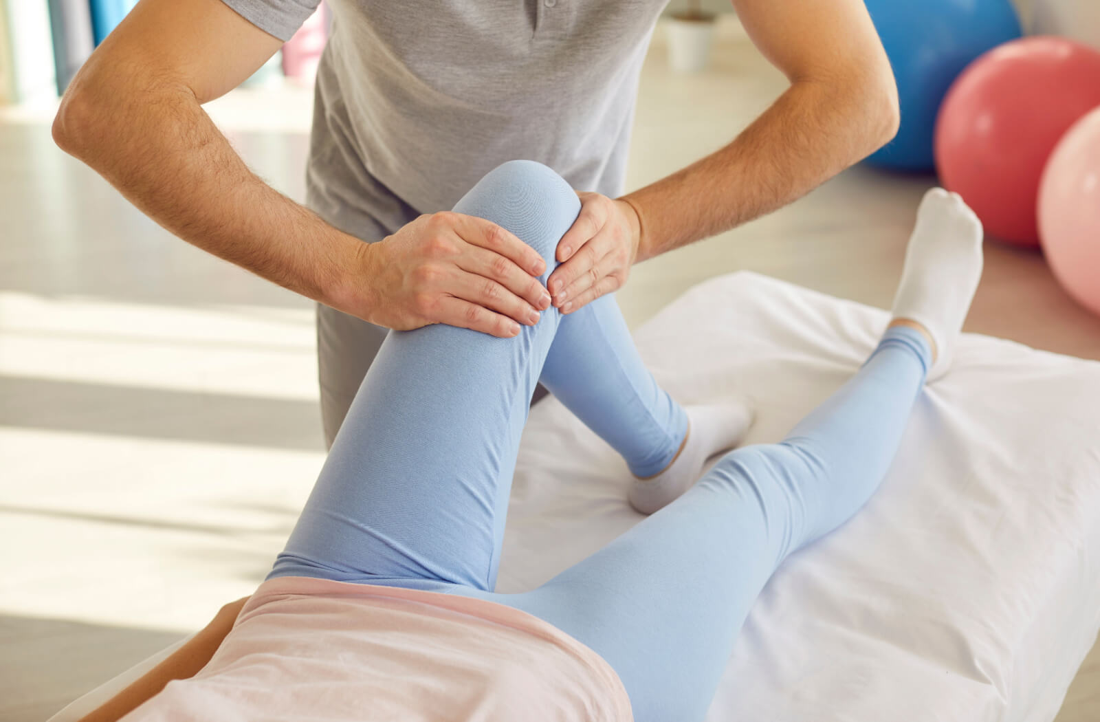 A massage therapist manipulates a patient's knee while the patient lies on a massage table.