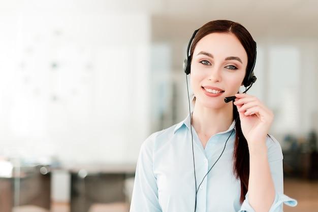 Smiling young office worker with a headset  answering in a call center, woman talking with clients. Portrait of an attractive customer and technical support representative