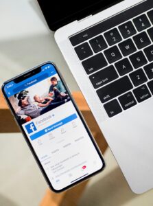 Building your personal brand on social media. Person using an iPhone X beside a MacBook on a wooden table.