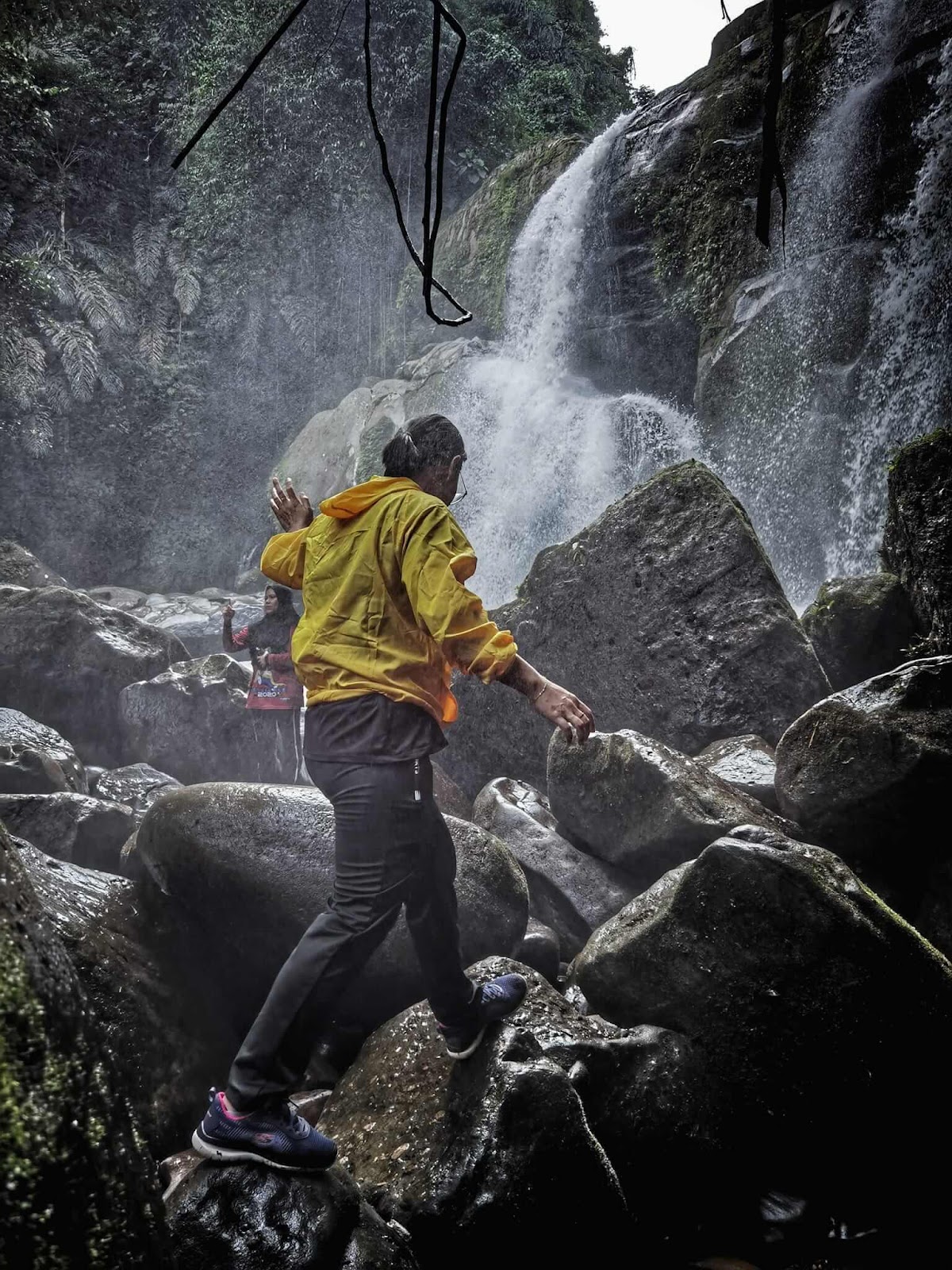 A person walking on rocks near a waterfall

Description automatically generated