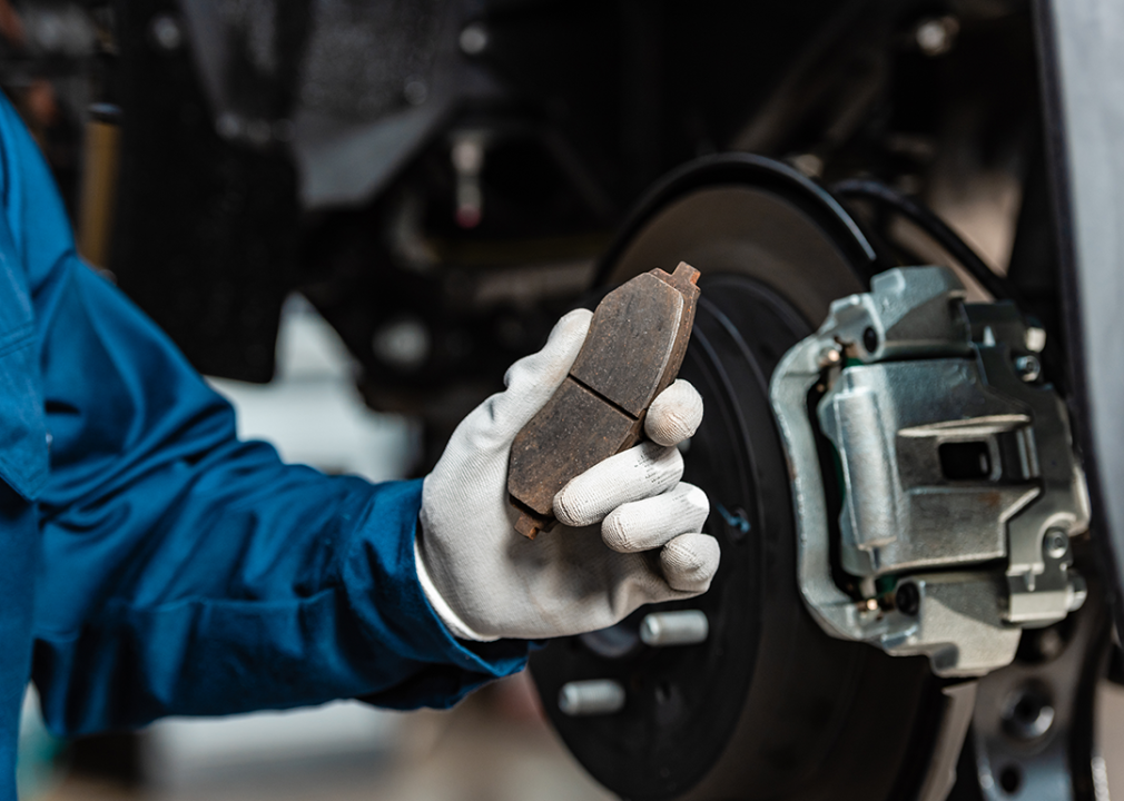 A mechanic holding a used brake pad near a wheel.
