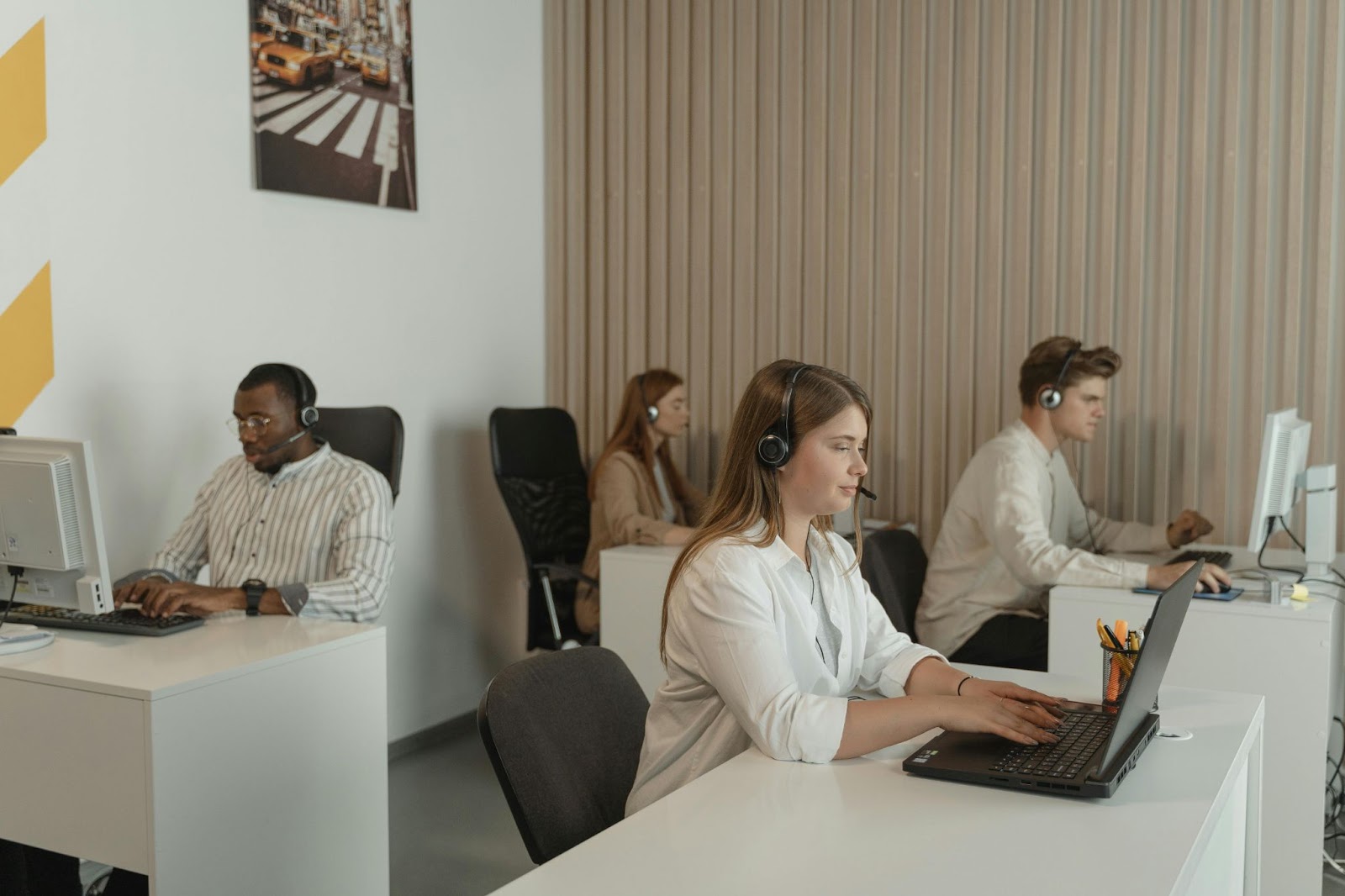 Customer service representatives work at their desks, wearing headsets and using computers.