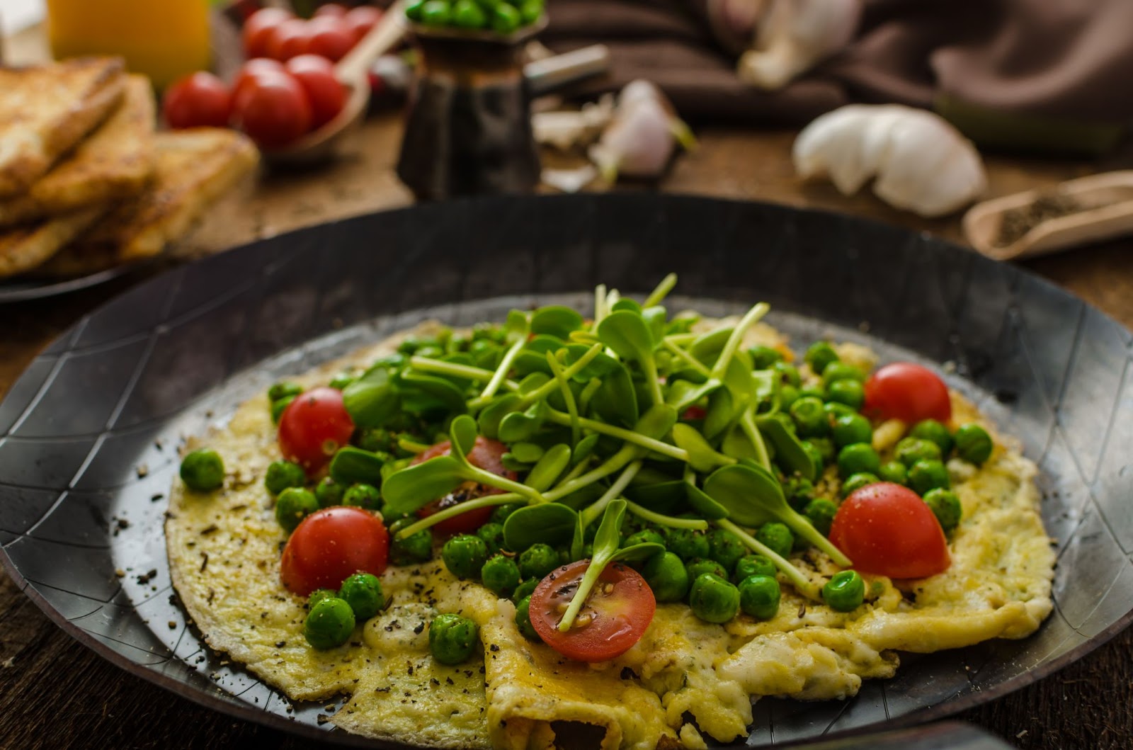 A close-up view of an omelette with veggies, microgreens and tomatoes as toppings.