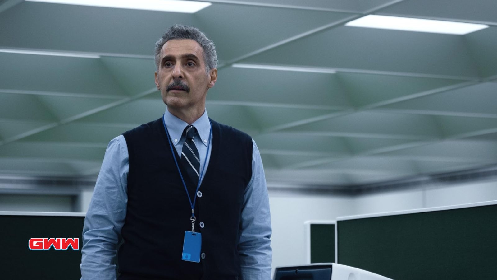 Irving with a serious expression, wearing a vest, in a minimalist office.