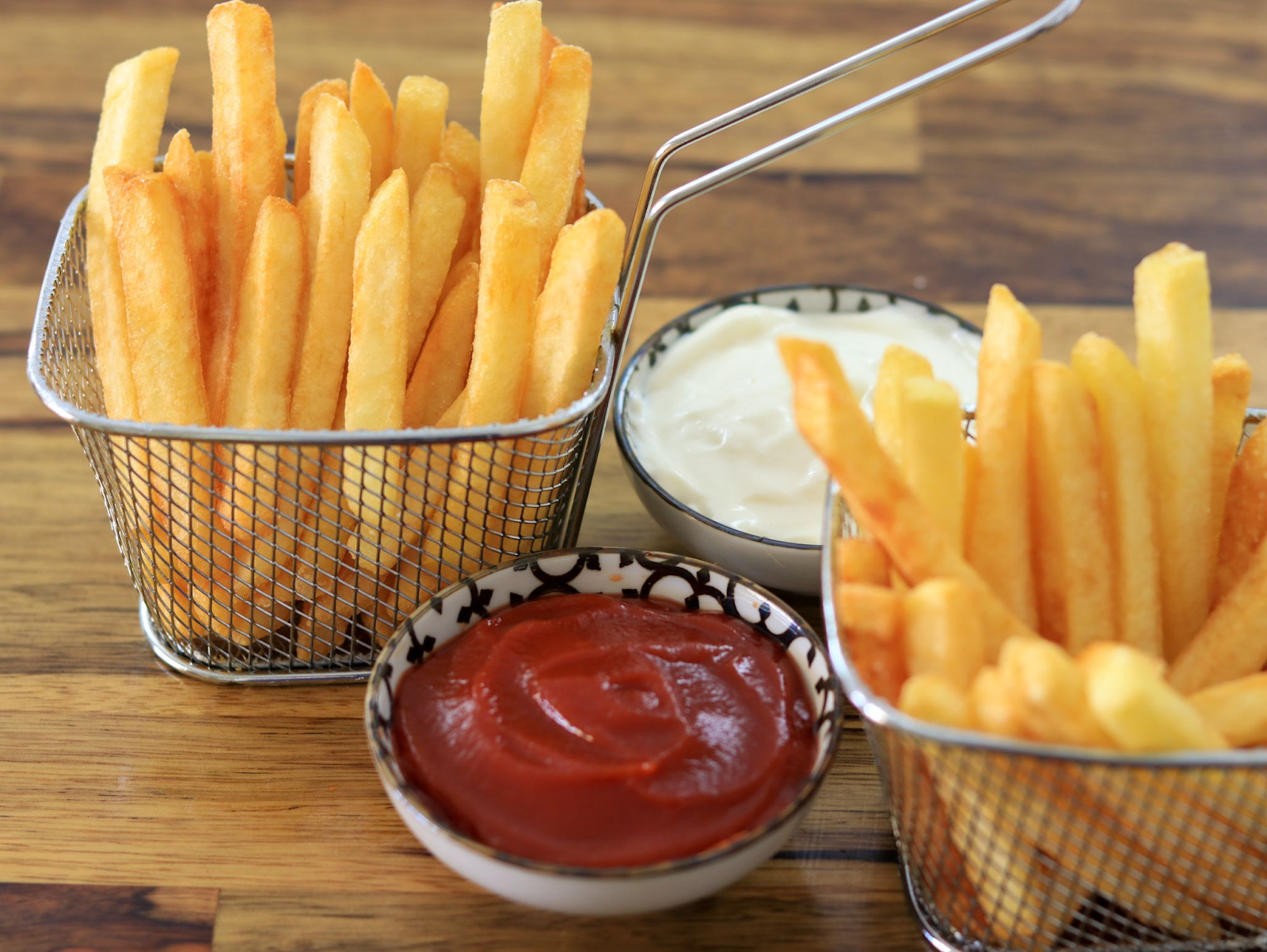 two baskets of French fries with mayo and ketchup 