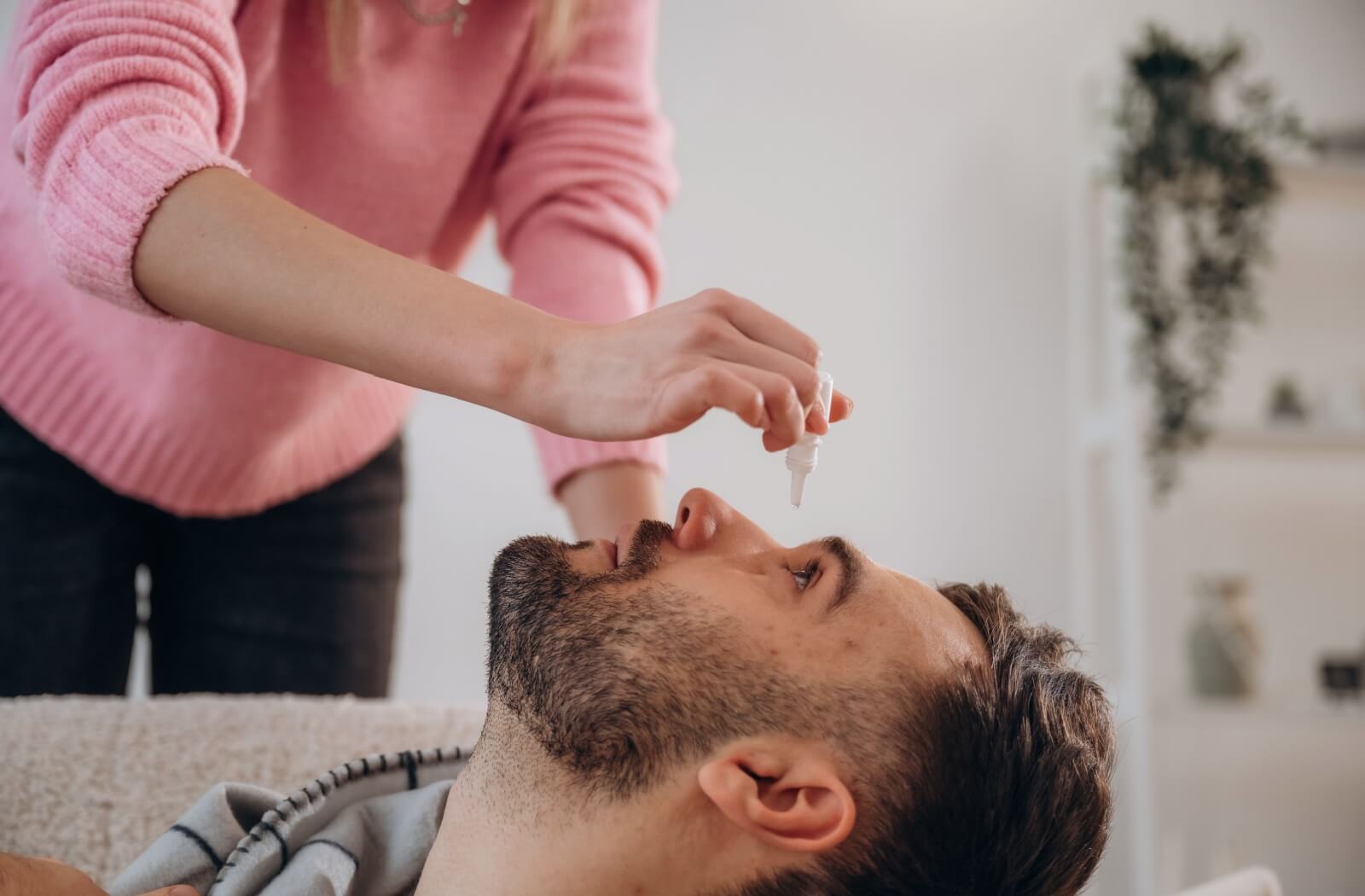  An adult leans back on a couch so their partner can apply eye drops to relieve post-LASIK dry eye symptoms at home.