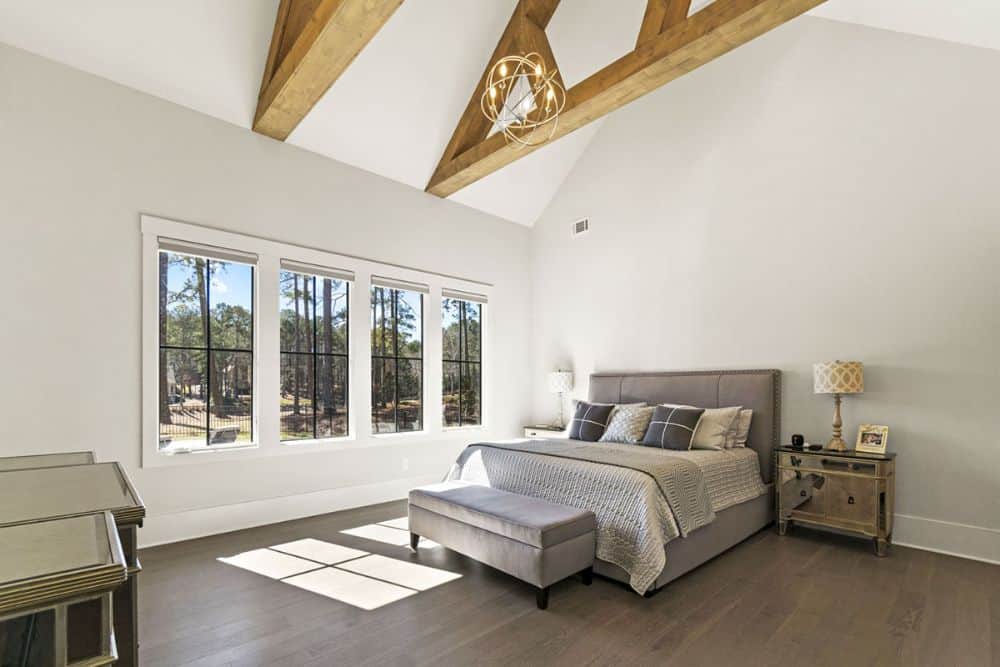 Primary bedroom with white walls, dark hardwood flooring, and a cathedral ceiling framed with exposed trusses.