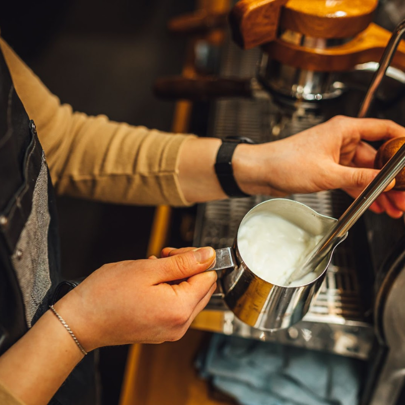 a barista steaming milk in a pitcher