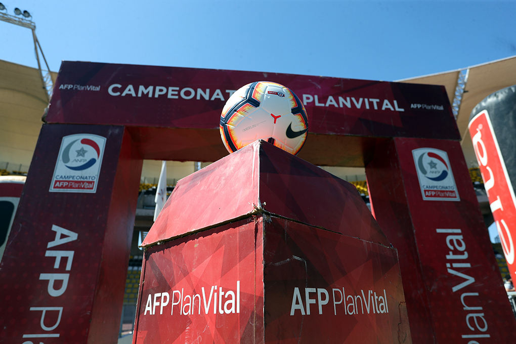 Balón de fútbol en un podio frente a un arco promocional del campeonato AFP PlanVital, en un estadio iluminado.