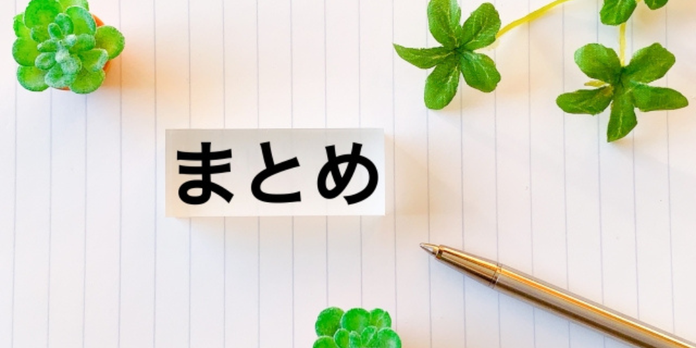 ノートの上に「まとめ」と書かれた紙とペン、まわりにクローバーや多肉植物が配置された構成