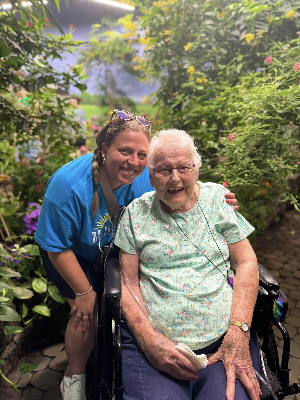 An inpatient facility resident smiling and embracing a caregiver against the backdrop of a lush floral scene.