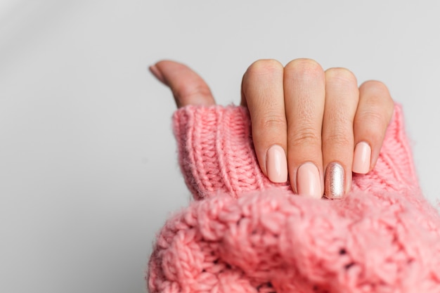 Manicure bonita cor nude, um dedo dourado brilhante, sobre fundo de malha de lã rosa