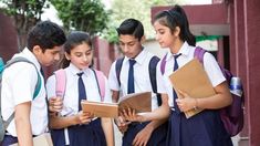 This contains an image of  four student in school uniforms are looking at something on a text book while one girl is holding a folder