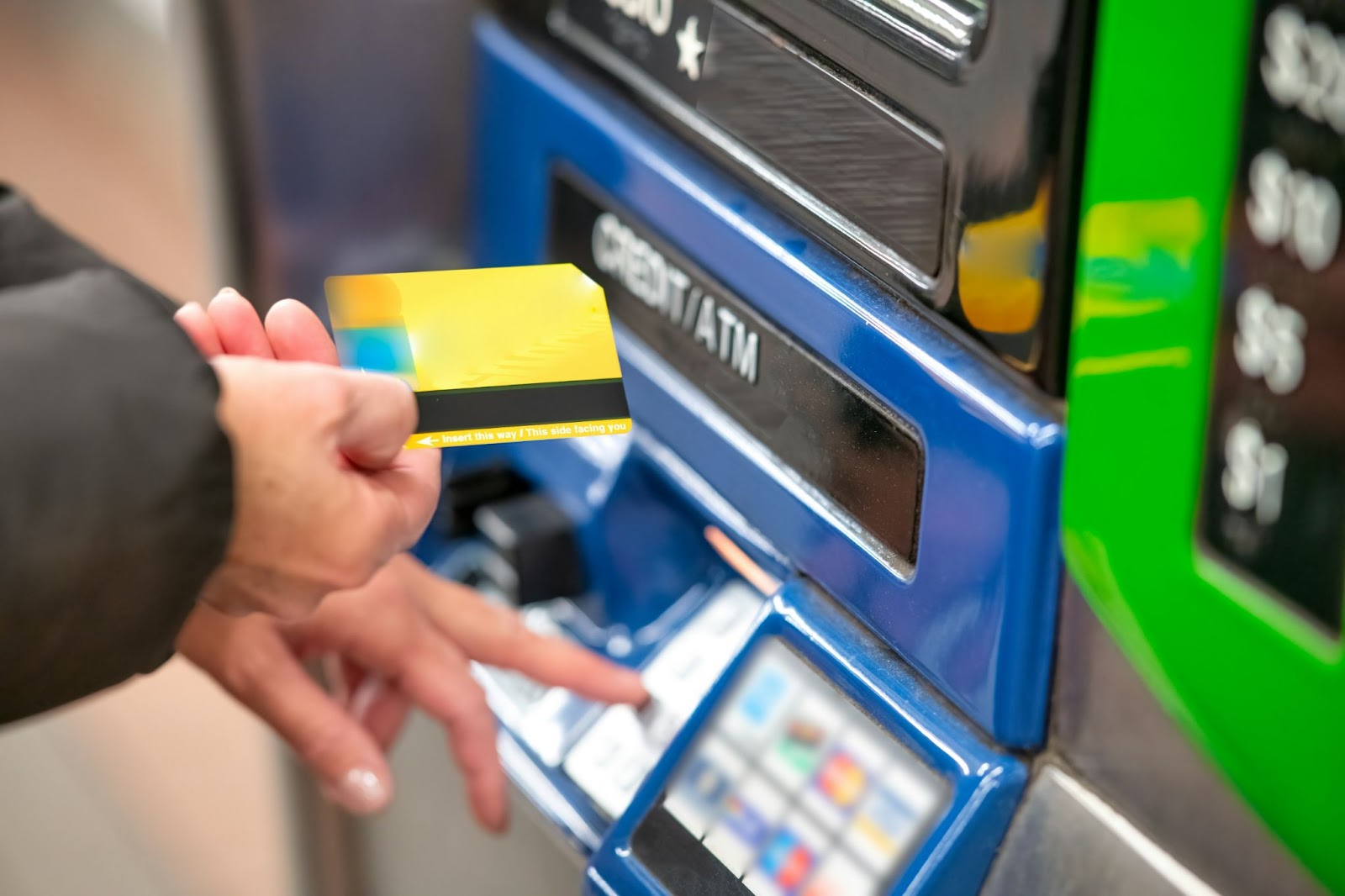 A person inserting a yellow credit card into a blue ATM machine