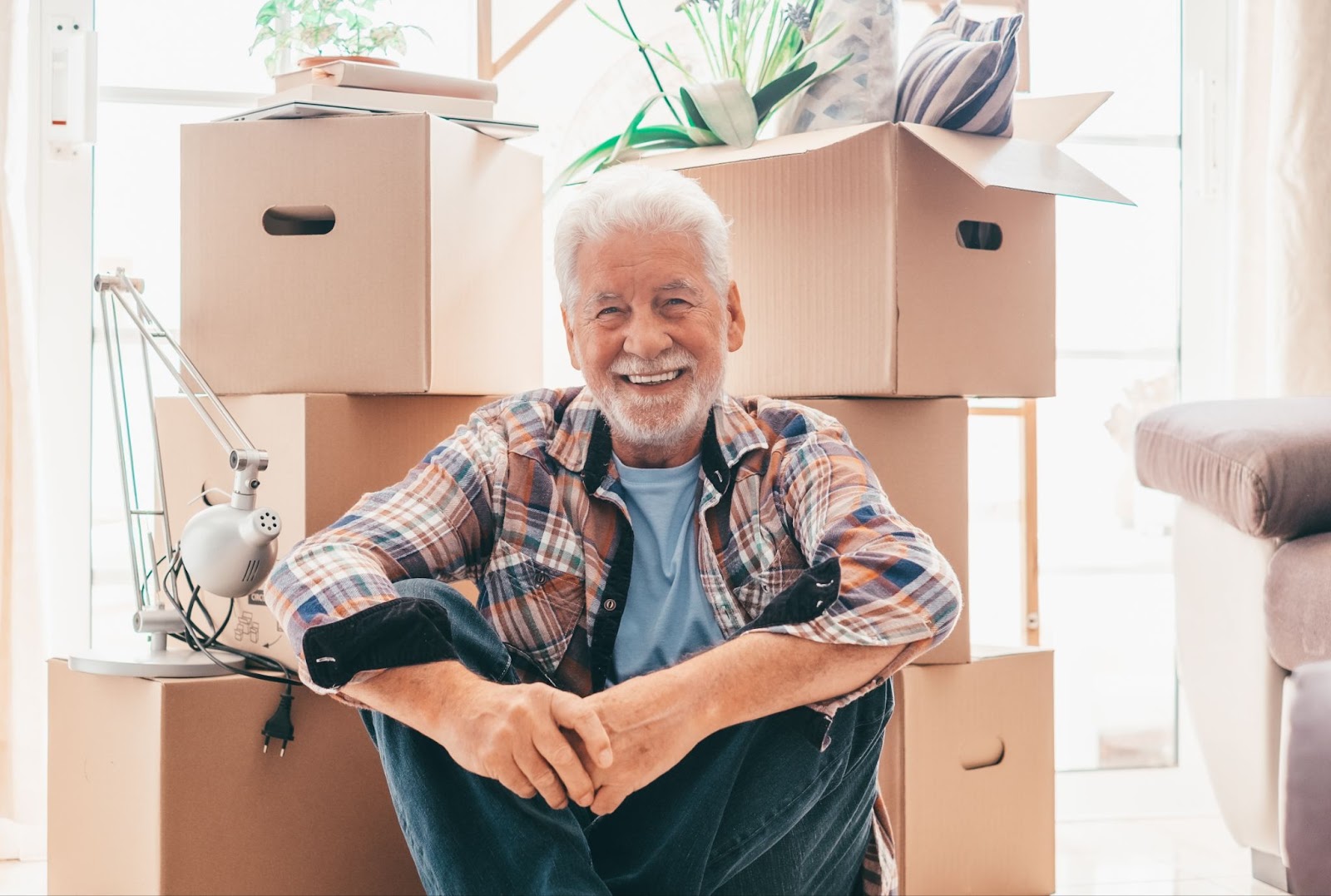  Happy older man sitting on the floor with moving boxes behind him.